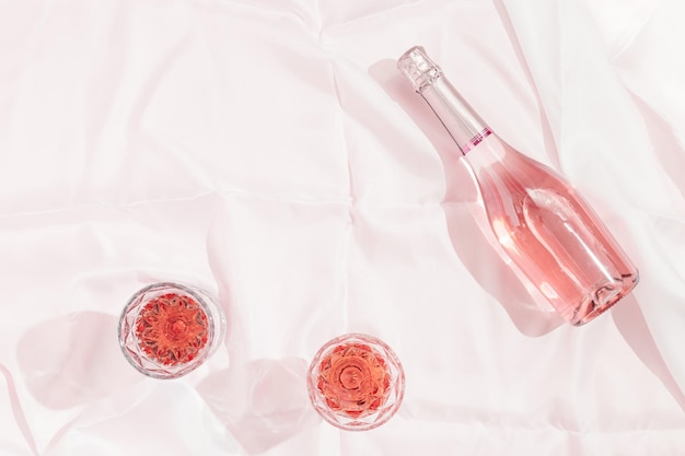 Bottle of rose champagne wine and two glasses with drink on white tablecloth in bright sunlight