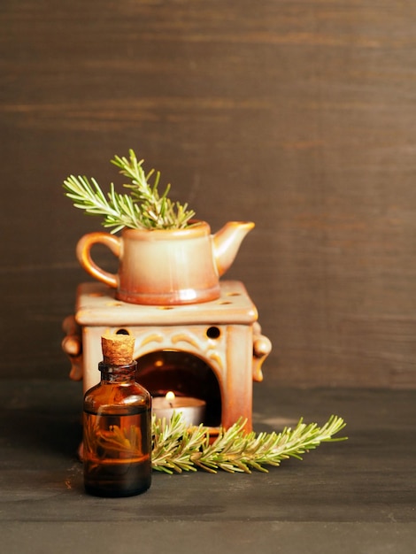 Bottle of rosemary essential oil with fresh sprigs of rosemary and aroma lamp