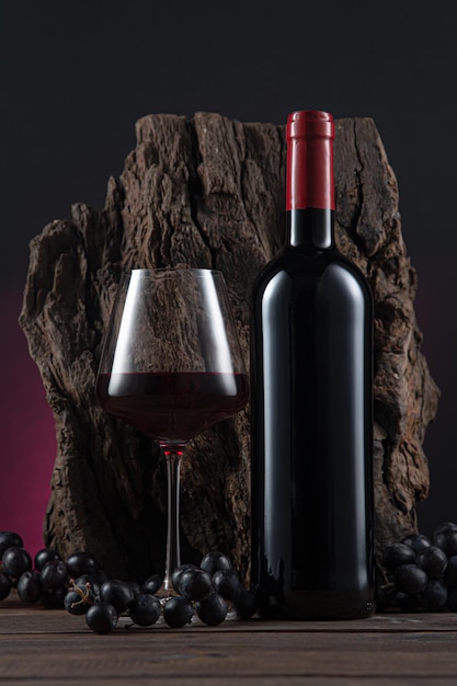 Bottle of spanish red wine and grapes on wooden base on black and red background vertical format
