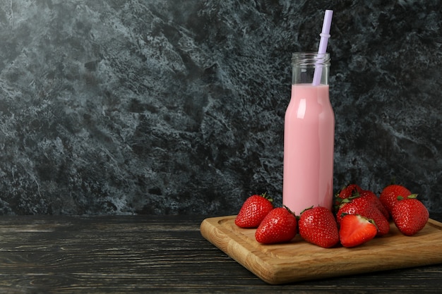 Bottle of strawberry milkshake and ingredients on wooden table\