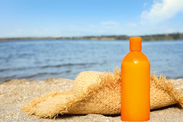 Bottle of sun protection body cream and hat on beach space for design