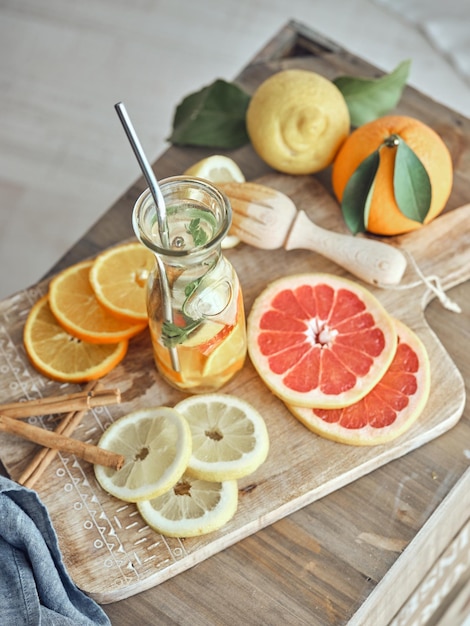 Bottle of tasty lemonade served with various sliced citrus fruits and cinnamon sticks on chopping board with whole lemon and orange on wooden table