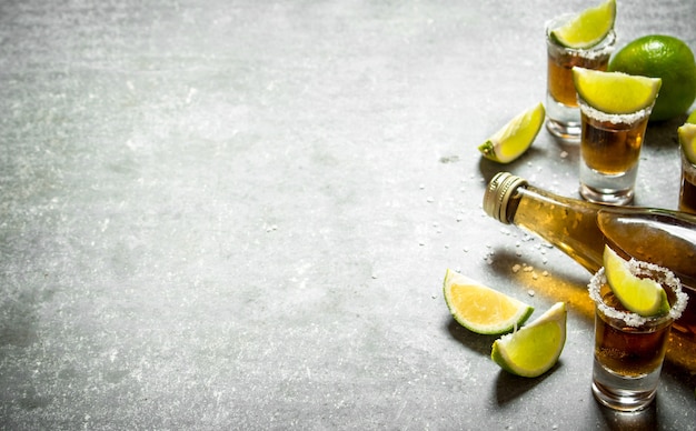 Photo bottle of tequila with lime and salt. on the stone table.