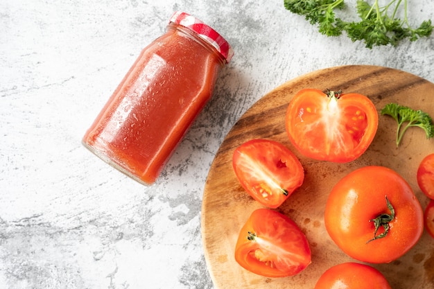 Bottle of tomato juice and fresh tomatoes on cement table background. Top view