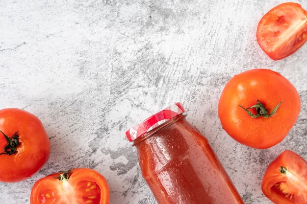 Bottle of tomato juice and fresh tomatoes on cement table background.