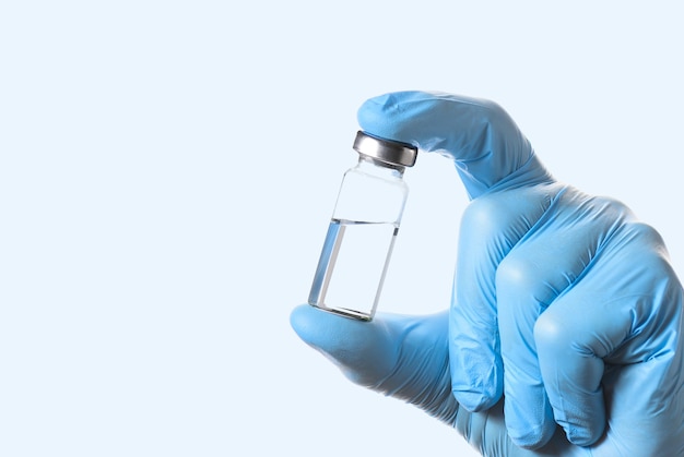 A bottle of vaccine for injection in the doctor's hand on a light blue background