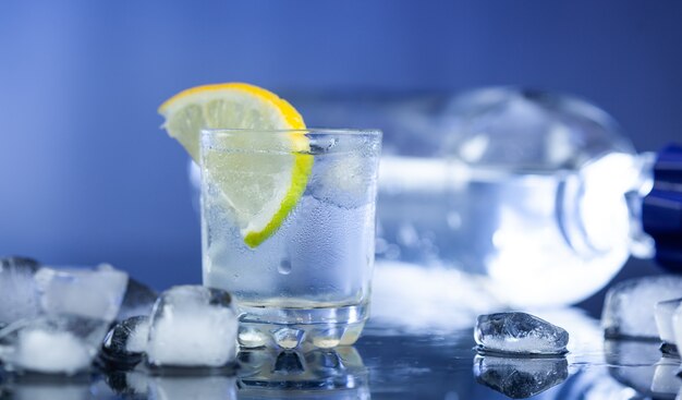 Bottle of vodka and glass with lemon on dark background