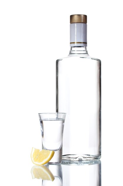 Bottle of vodka and wineglass with lemon isolated on white