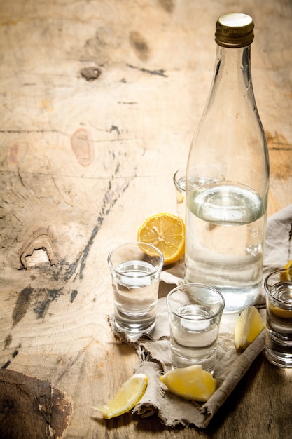 Bottle of vodka with shot glasses and lemon. On wooden background.