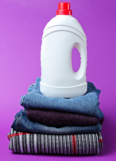 Bottle of washing gel on stack of clothes on purple table.