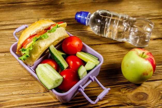 Bottle of water apple and lunch box with burgers and fresh vegetables on a wooden table