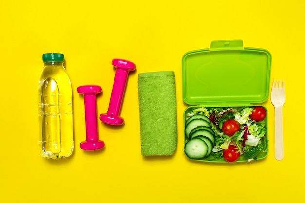 Photo bottle of water and dumbbells next to a salad