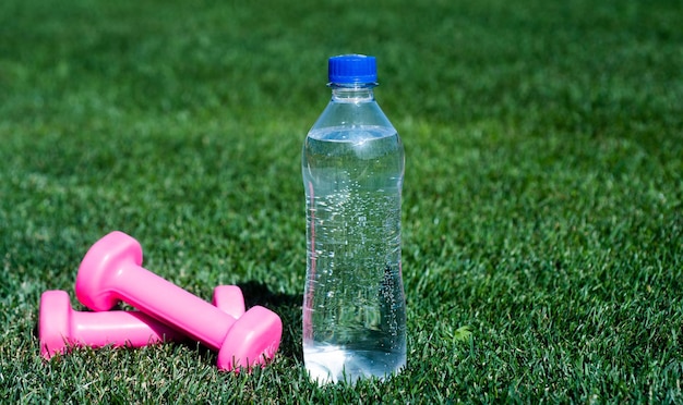 Bottle of water and fitness barbells on green grass hydration