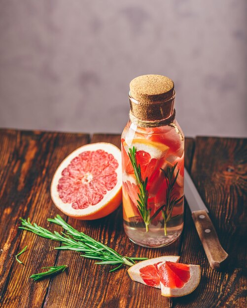 Bottle of water infused with sliced raw grapefruit and fresh springs of rosemary. vertical orientation.