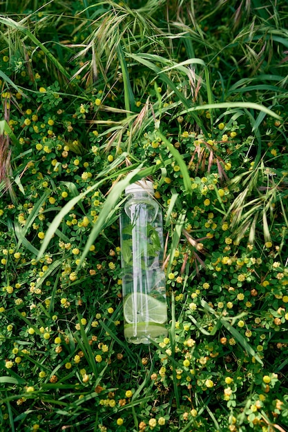 Bottle of water lies on the green tall grass among the wildflowers