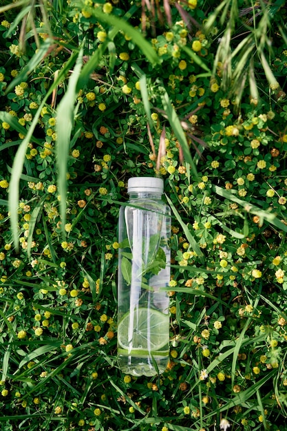 Бутылка воды лежит на зеленой высокой траве среди желтых полевых цветов.