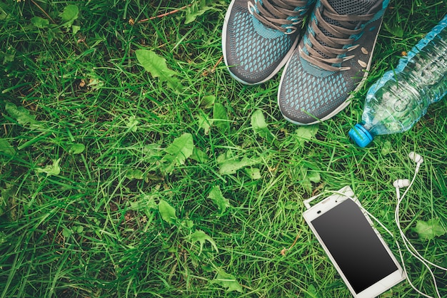 Bottle of water and sneakers on grass background