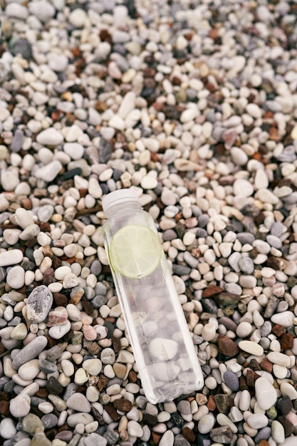 Bottle of water with a slice of lime lies on a pebble beach