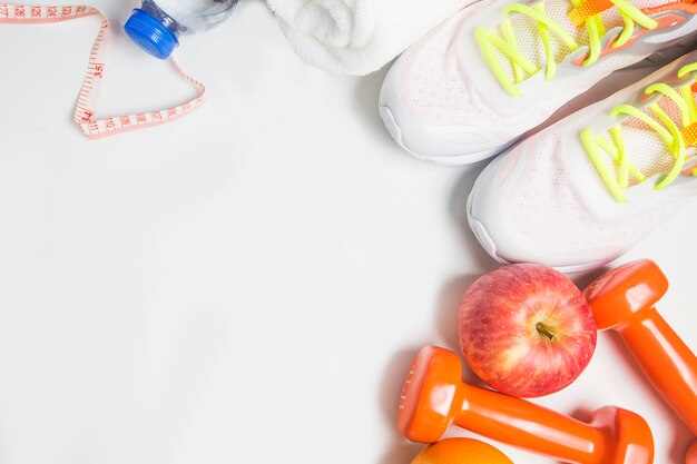 Bottiglia di acqua con scarpe da ginnastica e pesi e una mela