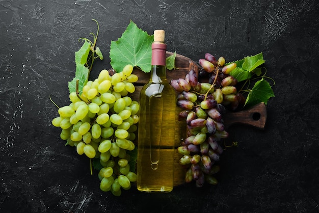 Bottle of white wine and fresh grapes on a black stone table Top view Free space for your text