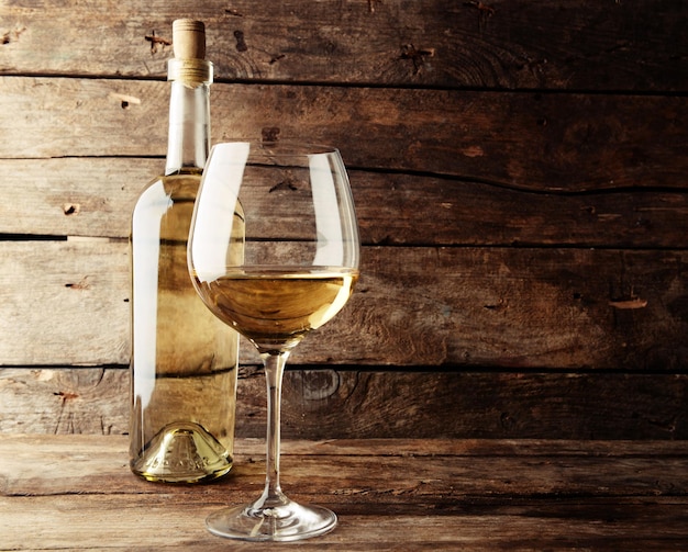 A bottle of white wine and a glass on wooden table