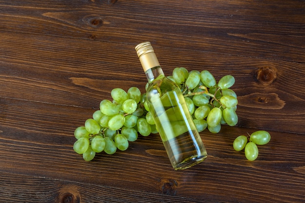 A bottle of white wine with grapes on a wooden background