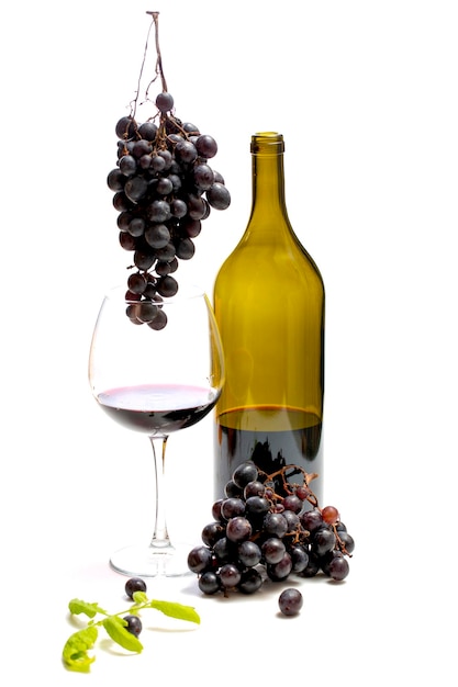 A bottle of wine and bunches of ripe grapes in a glass on a white background