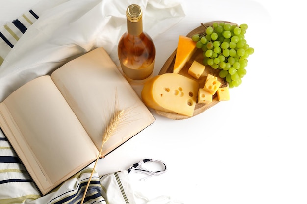 木の板のタリットトラのワインチーズスライスとブドウのボトルイスラエルの休日シャブオットの概念