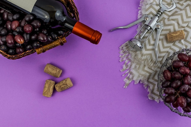 Bottle of wine, fresh ripe grapes, corks, and corkscrew on purple background