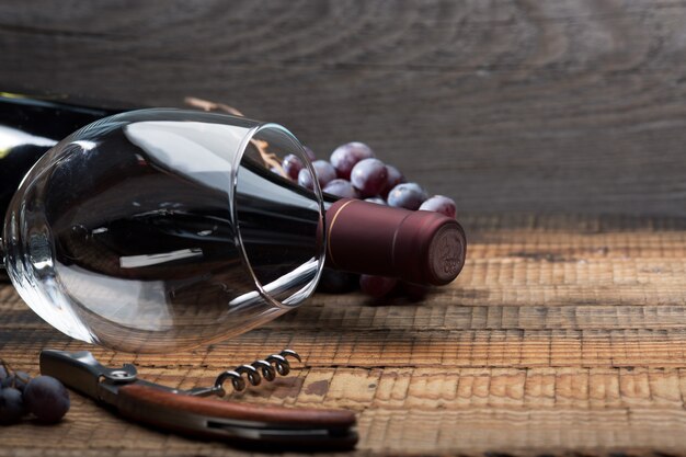 bottle of wine, a glass, a bunch of grapes and grape leaves on an old wooden table.