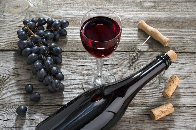 Bottle of wine,  glass of wine and  bunch of blue grapes on gray wooden table. Top view.