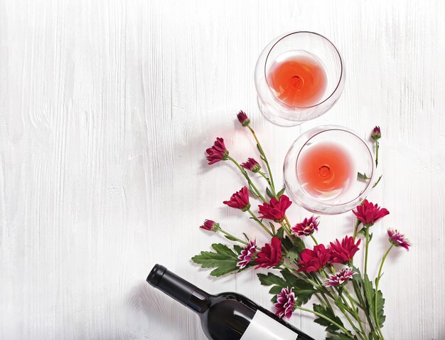 Bottiglia di vino, bicchieri e fiori su uno sfondo di legno