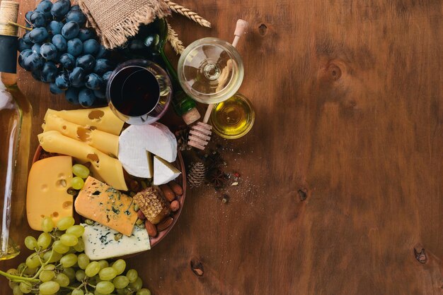 A bottle of wine and a large assortment of cheeses honey nuts and spices on a wooden table Top view Free space for text