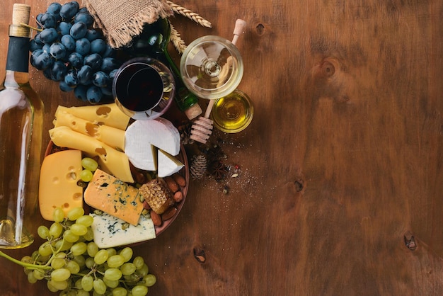 A bottle of wine and a large assortment of cheeses honey nuts and spices on a wooden table Top view Free space for text