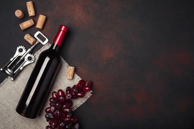 Bottle of wine, red grapes, corkscrew and corks, on rusty background top view