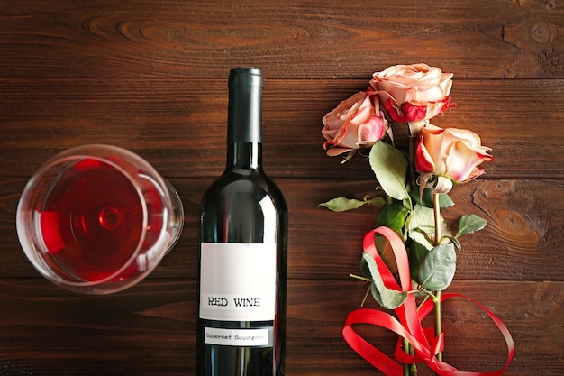 Bottle of wine and roses on a wooden background