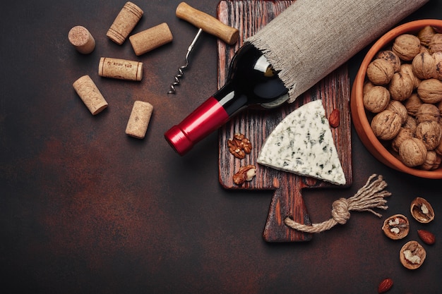 Bottle of wine, walnut, blue cheese, almonds, corkscrew and corks, on rusty background top view