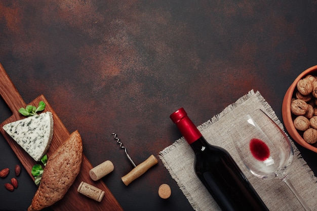 Bottiglia di vino, noci, formaggio blu, mandorle, cavatappi e tappi di sughero, su fondo arrugginito vista dall'alto