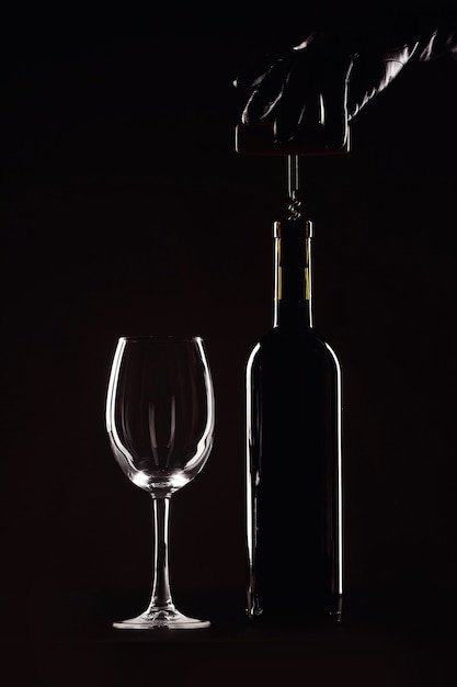 Bottle of wine with a glass on a black background, corkscrew