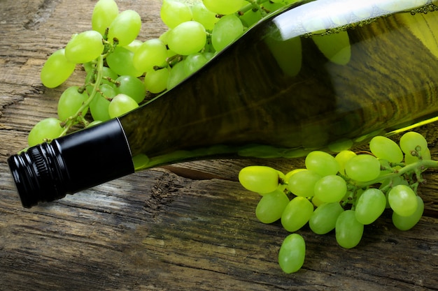 Bottle of wine with grapes on wooden table.