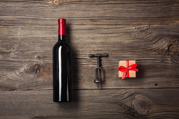 Bottle of wine with wine glass and gift box on wooden background. Top view with copy space for your text.