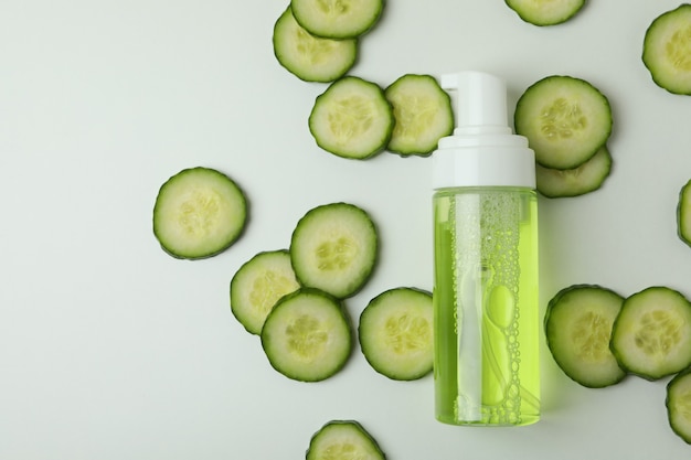 Bottle with cosmetics and cucumber slices on white surface