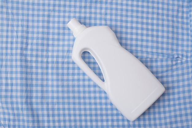 Bottle with detergent on a blue checkered clothes. Top view.