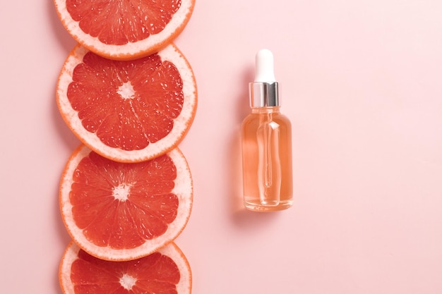 Bottle with dropper of aroma essential oil wich grapefruit fresh slice Flat lay top view face serum in bottle on pink table SPA relax face skin care and body treatment