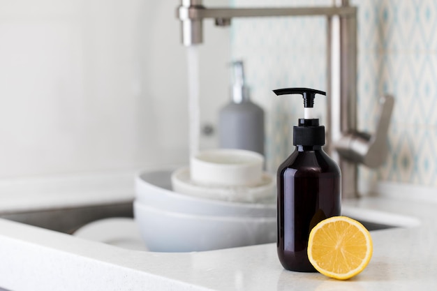 Bottle with eco friendly dishwashing detergent with lemon on the background of a sink with dirty dishes