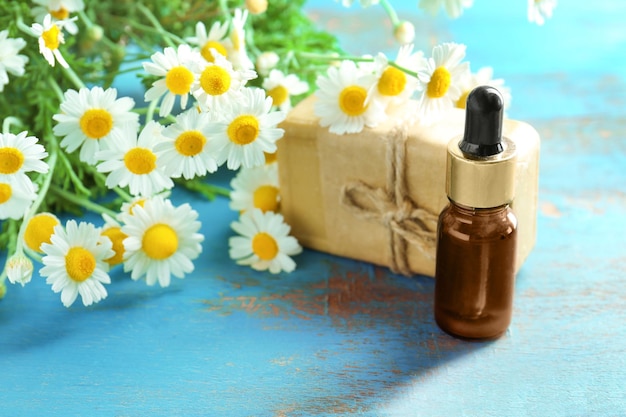 Bottle with essential oil soap and chamomile flowers on wooden table