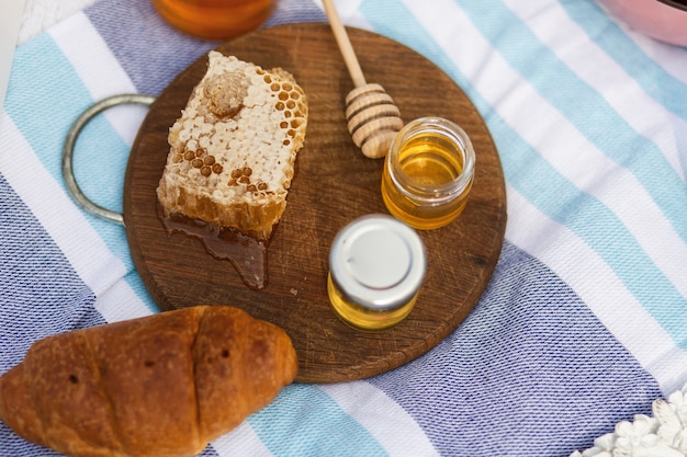 Bottiglia con miele, bagel e nido d'ape su un piatto di legno.