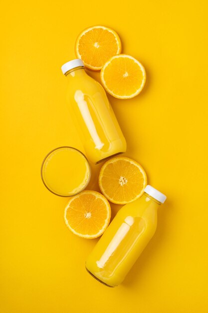 Bottle with juice and oranges on a yellow background