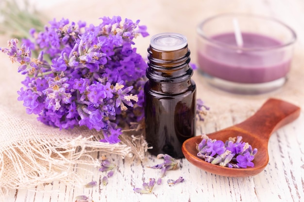 Una bottiglia con olio di lavanda e delicati fiori di lavanda su sfondo bianco