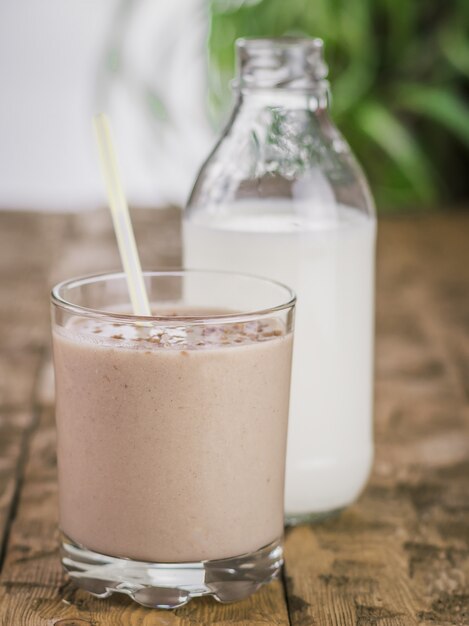 Bottle with milk and chocolate smoothie with banana and pear on a wooden table.